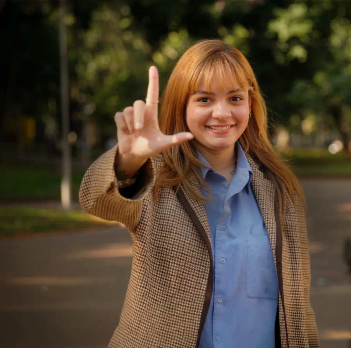 Jovem sorrindo e fazendo o gesto da letra L com a mão